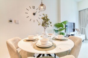 A dining area with a round table, chairs, a wall clock, a potted plant, and a television.