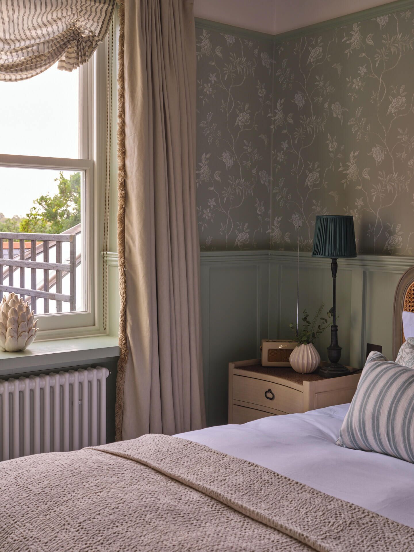 A bedroom with a bed, a nightstand, a lamp, and a window with curtains.