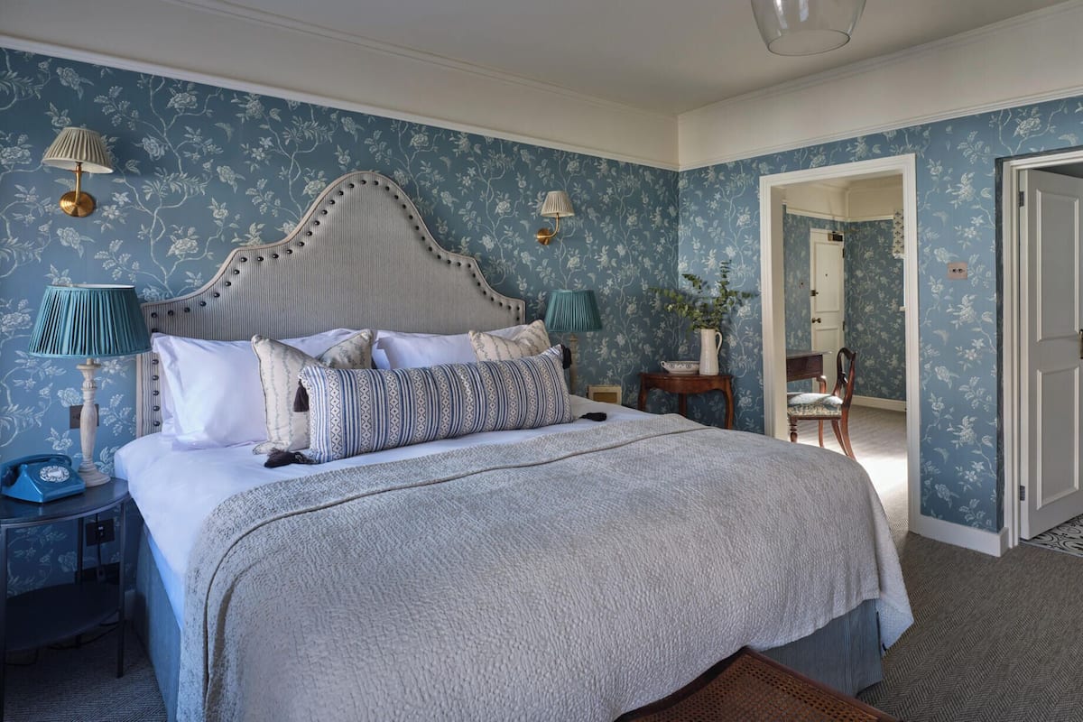 A bedroom with a large bed, two bedside tables with lamps, a wooden chair, and a door leading to another room.