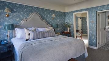 A bedroom with a large bed, two bedside tables with lamps, a wooden chair, and a door leading to another room.