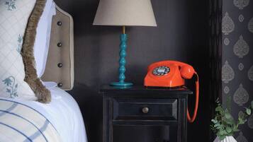 En pænt redt seng med knægt, et lille natbord med lampe, en orange telefon og en dekorativ vase.