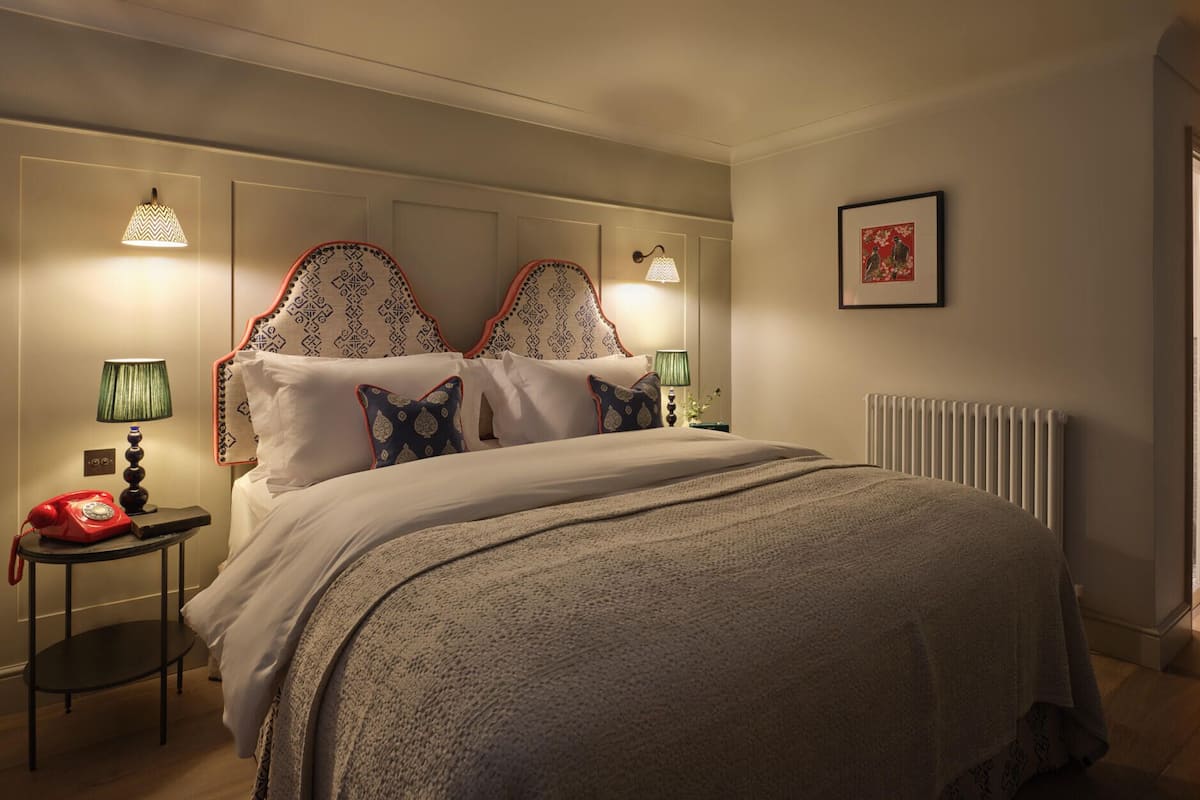 A neatly made bed with a patterned headboard, a bedside table with a lamp, and a framed picture on the wall.