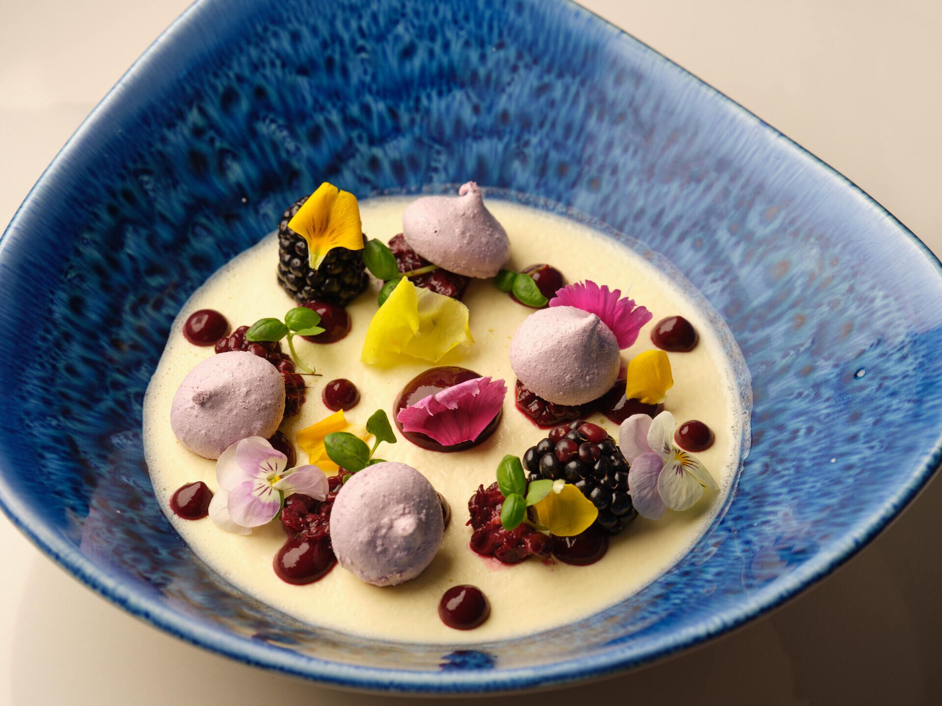 A dessert with various berries and flowers on a blue ceramic plate.