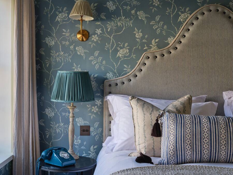 A neatly made bed with patterned pillows, a bedside lamp, and a vintage telephone on a small table beside the bed.