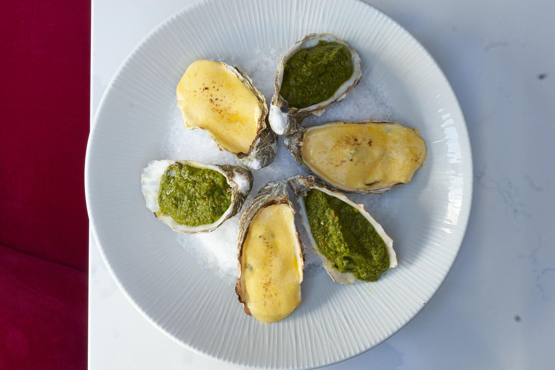 A plate with six oysters, some with green sauce.