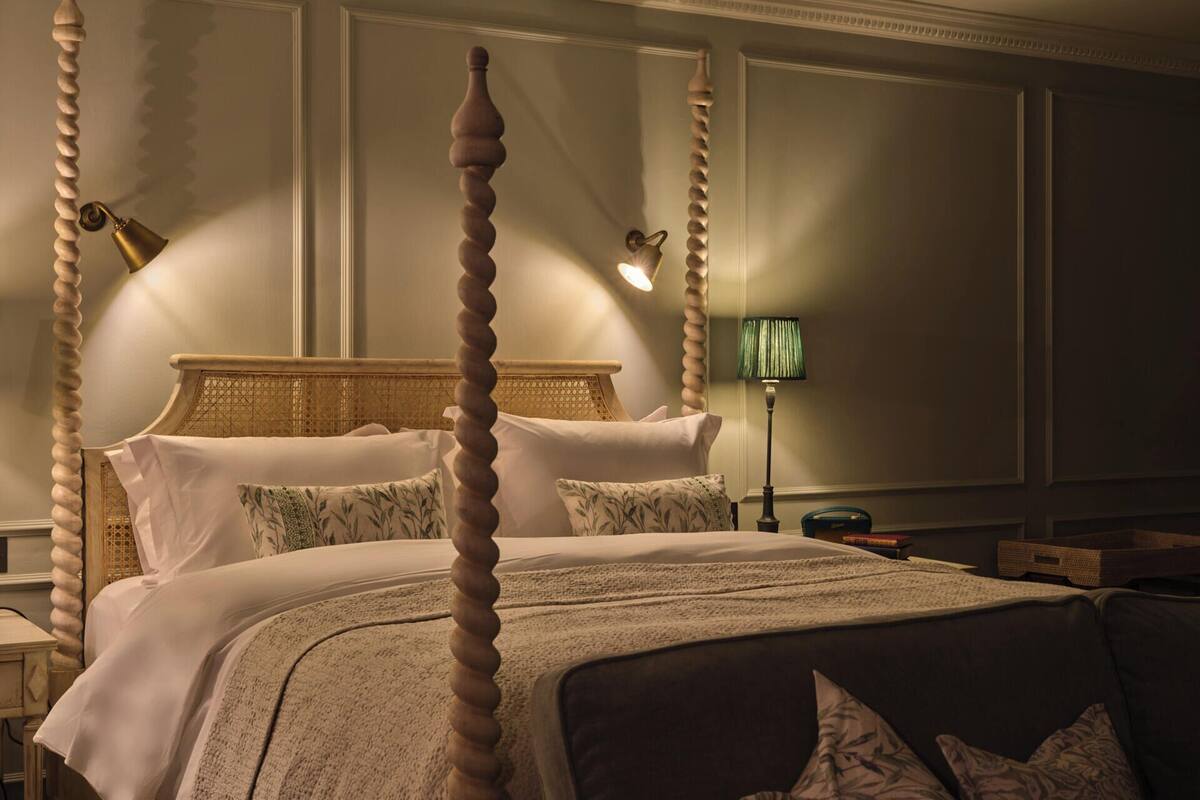 A four-poster bed with a woven headboard, a green floor lamp, and a bedside table with a lamp.