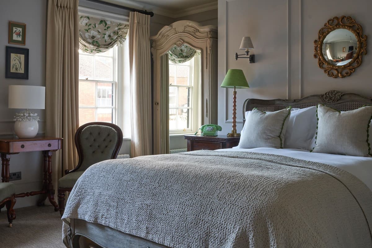 A classic bedroom with a large bed, a chair, a nightstand, a lamp, and a mirror.