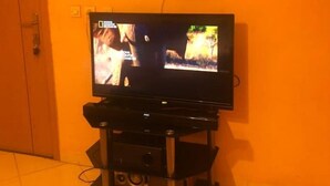 Un televisor sobre un mueble en una habitación con pared naranja y puerta de madera.