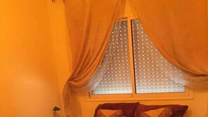 Un dormitorio con cama, cortinas, una ventana con persianas y mesitas de noche.