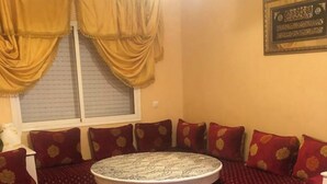 Una habitación con una mesa redonda, un sofá de color rojo con diseño y cortinas amarillas.