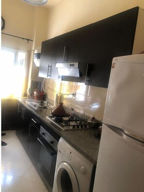 A compact kitchen with a gas stove, a built-in oven, a washing machine, and a refrigerator.