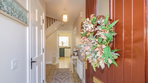 A hallway with a wooden door, a rug, a staircase, and a kitchen area in the background. - Owen Tucker View House (Ardara)
