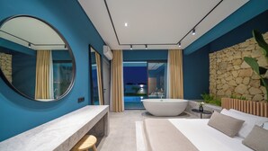 Une salle de bain moderne avec une grande baignoire, un miroir rond et un mur d’accent en pierre.