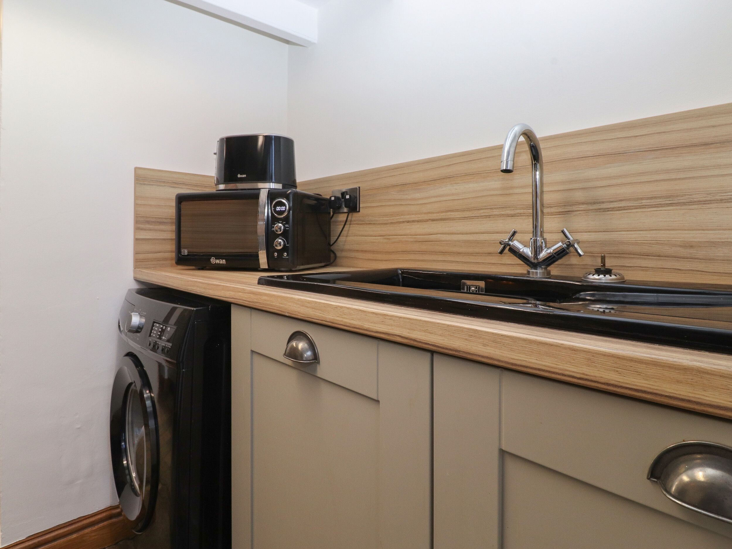 A compact kitchen with a microwave, toaster, sink, and washing machine.