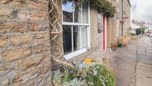 A stone building with a window, a red door, and a stone bench outside. - Wether Fell View (Hawes)