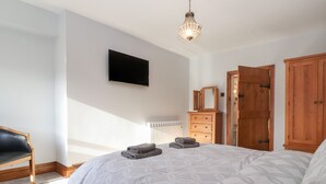 A bedroom with a large bed, a wooden dresser, a television mounted on the wall, and a wooden wardrobe. - Wether Fell View (Hawes)