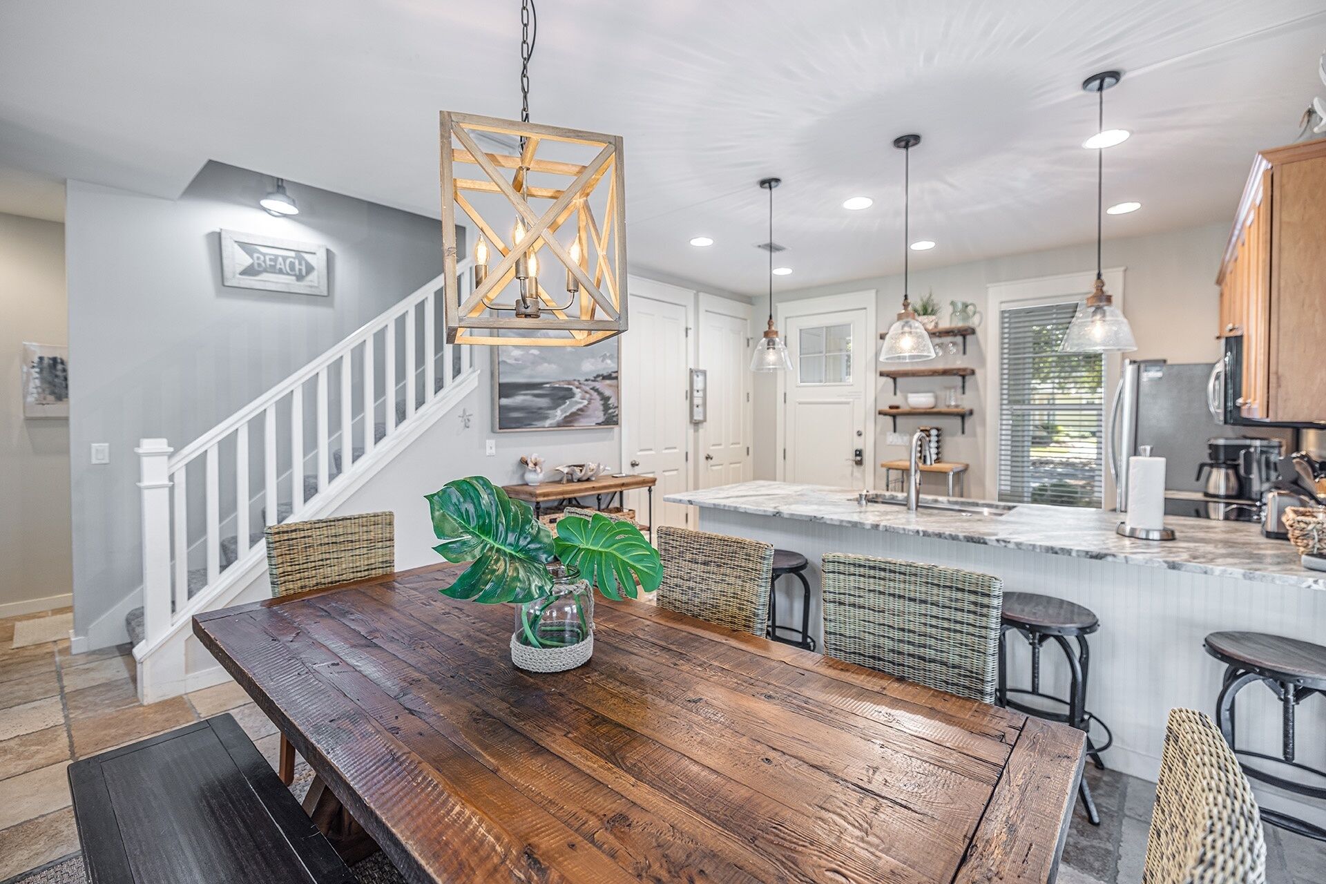 A spacious kitchen with a wooden dining table, wicker chairs, and pendant lighting.