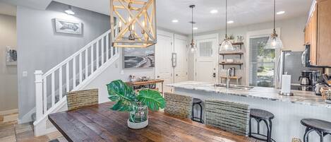 A spacious kitchen with a wooden dining table, wicker chairs, and pendant lighting.