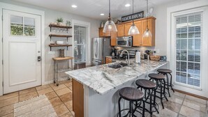 A modern kitchen with wooden cabinets, a marble island, bar stools, and pendant lighting. - 1364 Laurel Grove 3 Bedroom Home by RedAwning (Miramar Beach)