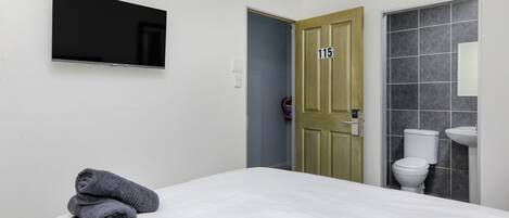 Ein Hotelzimmer mit einem Bett, einem an der Wand montierten Fernseher, einem Badezimmer mit Toilette und Waschbecken sowie einer Tür mit der Nummer 115.