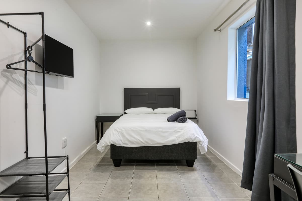 A small, modern bedroom with a bed, a TV mounted on the wall, and a window with curtains.