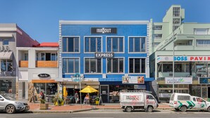A blue building with "INN & OUT" and "EXPRESS" signs, a "Sushi Bar" sign, and a "Coke" sign. - Inn & Out Express Sea Point (Cape Town)