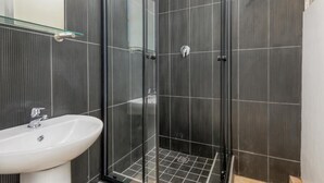 A modern bathroom with a glass-enclosed shower, a white sink, and dark tiled walls. - Inn & Out Express Sea Point (Cape Town)