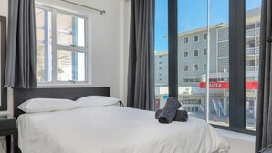 A hotel room with a large bed, a nightstand, and a window with curtains. - Inn & Out Express Sea Point (Cape Town)