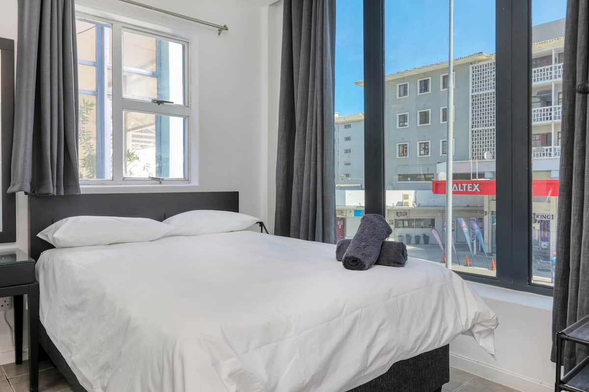A hotel room with a large bed, a nightstand, and a window with curtains.