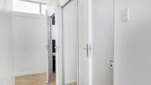 A hallway with white walls and a tiled floor, leading to a room with a door. - Inn & Out Express Sea Point (Cape Town)