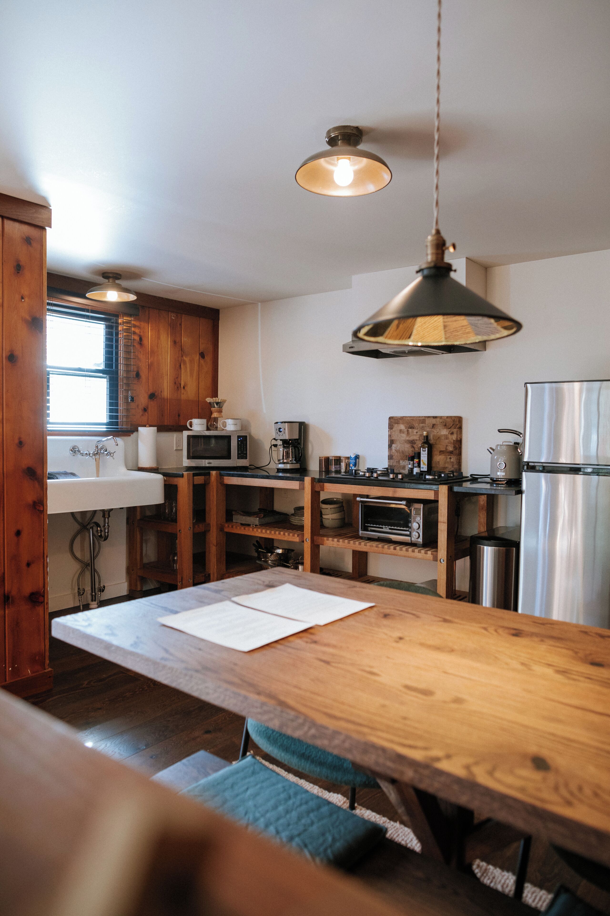 Eine Küche mit Holzschränken, einem Edelstahlkühlschrank, einer Mikrowelle, einer Kaffeemaschine und einem Holzessttisch mit Stühlen.