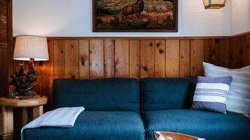 Una sala de estar acogedora con un sofá azul, una mesa redonda de centro, una lámpara y un cuadro en la pared.