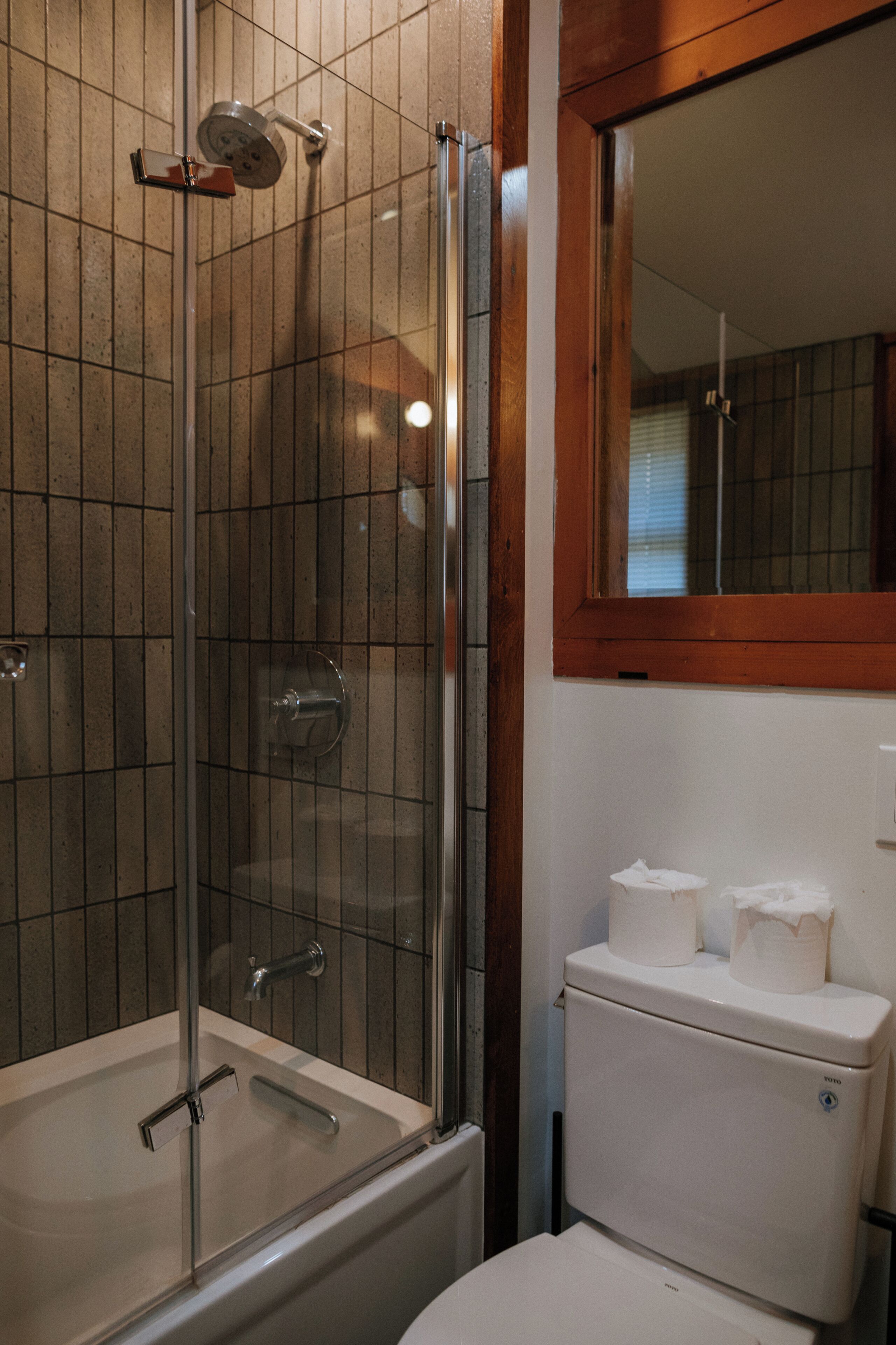 Un baño con ducha envuelta en vidrio, inodoro blanco y espejo sobre el lavamanos.