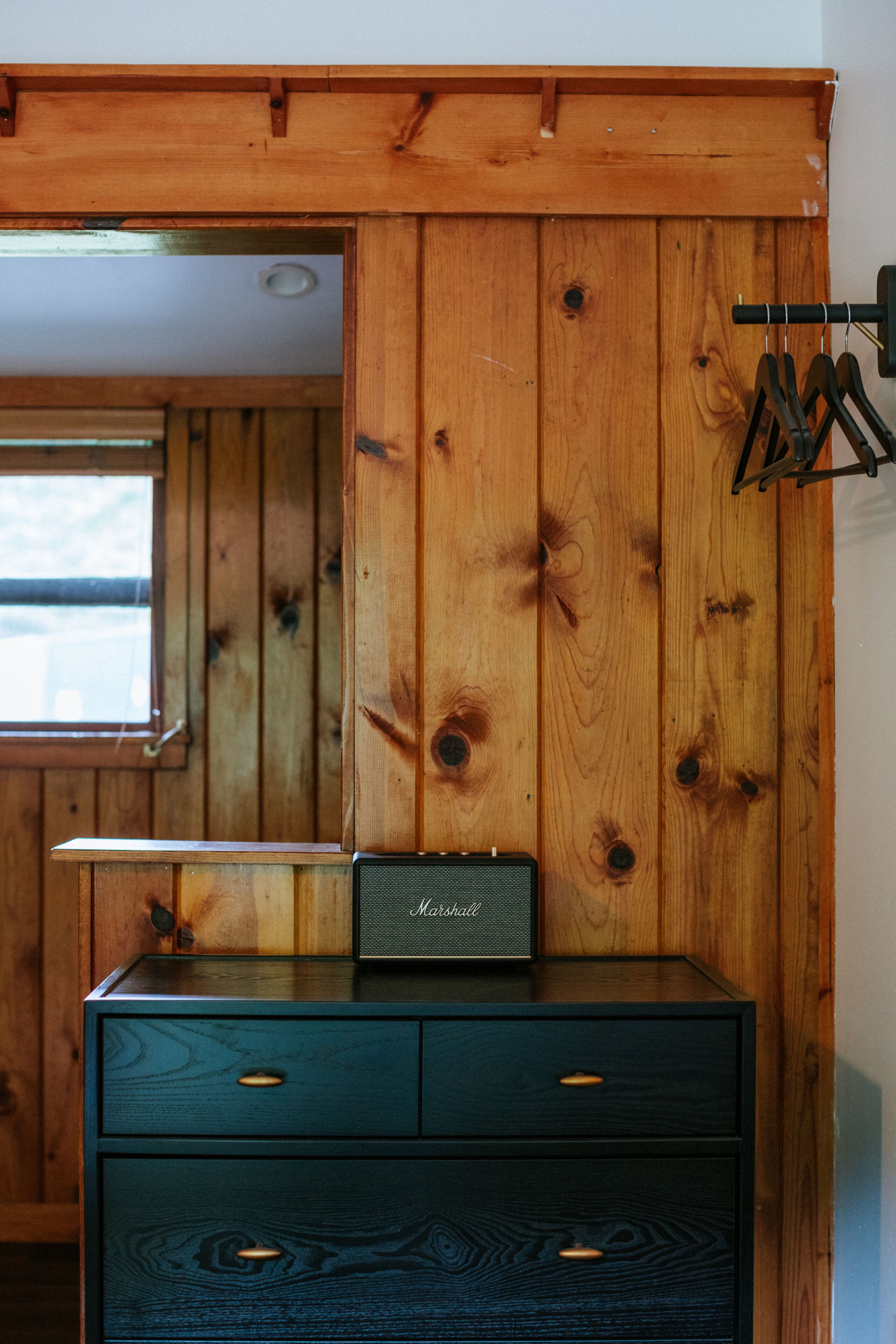 Une commode en bois, une radio, une fenêtre et un porte-manteau.