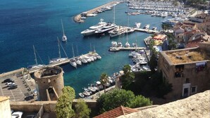 Un puerto costero con numerosas embarcaciones amarradas, una torre histórica y vistas del pueblo circundante.