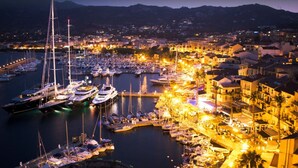 Un puerto deportivo con numerosas embarcaciones amarradas, rodeado de edificios y una zona costera bien iluminada.