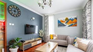 A modern living room with a flat-screen TV, a wooden coffee table, a grey sofa, and a painting on the wall.