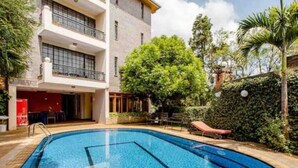 A hotel with a swimming pool, outdoor seating, and a multi-story building with balconies.