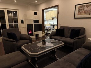 A living room with a fireplace, two sofas, a coffee table, and a dining area in the background.