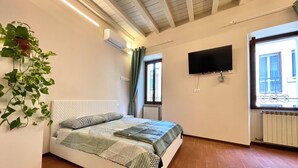 A bedroom with a bed, a TV, a window with curtains, and a radiator. - 40 m2 studio in the center of Brescia, 90 m from parking, no ZCL (Brescia)