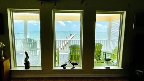 A room with three windows overlooking a beach, each with a chair and a small sculpture. - Wake Up to a Beautiful View! 3bdrm, 2 bath. Private Fishing Pier. (Port Mansfield)