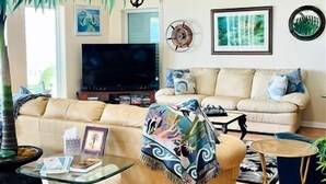 A living room with a beige sofa, a glass coffee table, a TV, and a decorative anchor on the wall. - Wake Up to a Beautiful View! 3bdrm, 2 bath. Private Fishing Pier. (Port Mansfield)