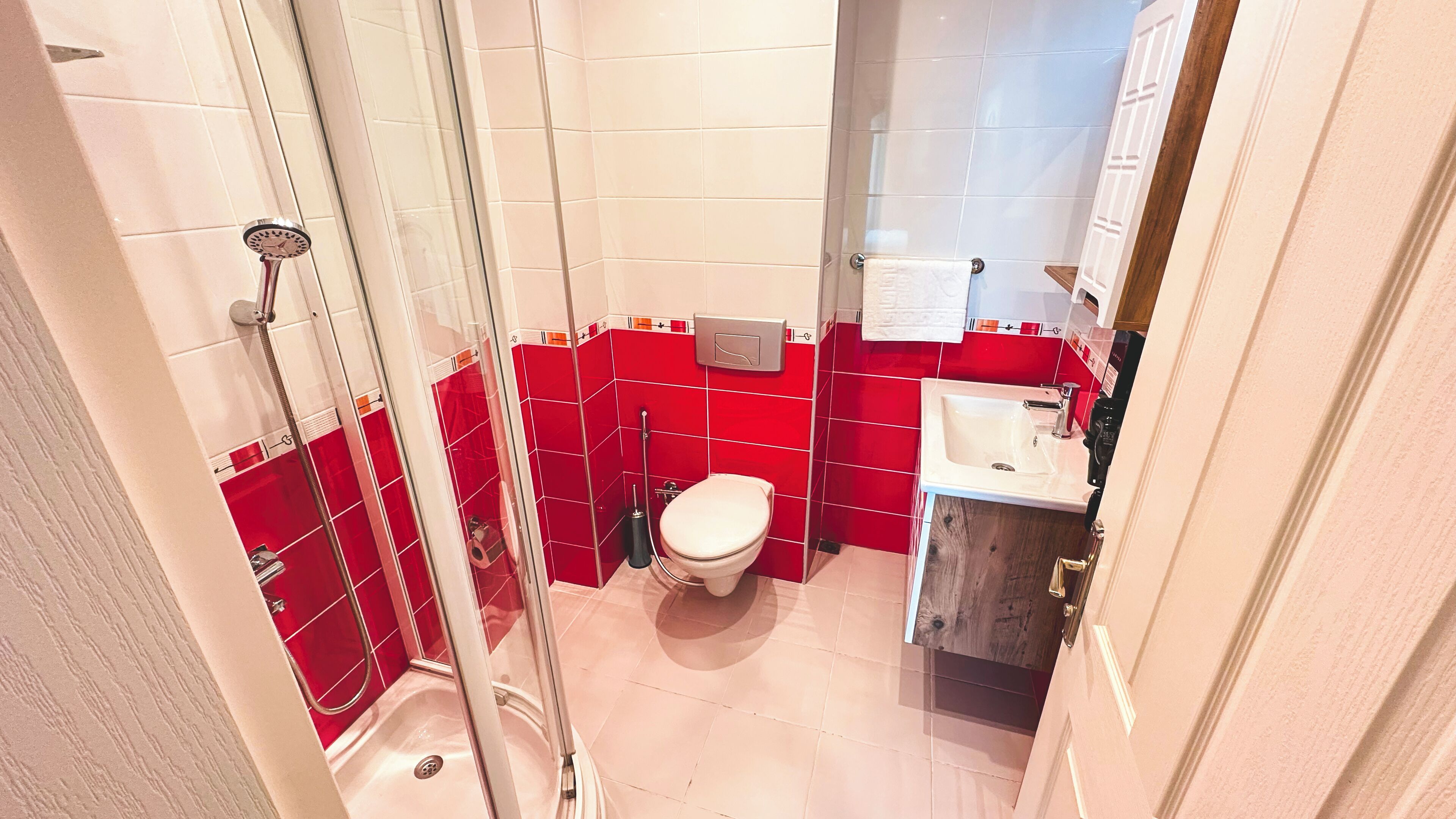 Une salle de bain avec douche, toilettes, lavabo et murs recouverts de carreaux rouges.