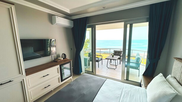 Habitación de hotel con cama, televisión, escritorio con cafetera y puerta corrediza de vidrio que da a un balcón con vista al océano.