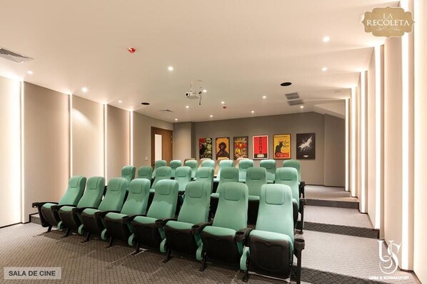 A cinema room with rows of teal and black seats, a projector, and framed artwork on the wall.
