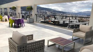 Een terras op het dak met buitenmeubilair, een stadsgezicht en een hekwerk.