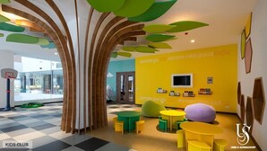 Een speelruimte voor kinderen met kleurrijk meubilair en een gele muur met educatieve posters.