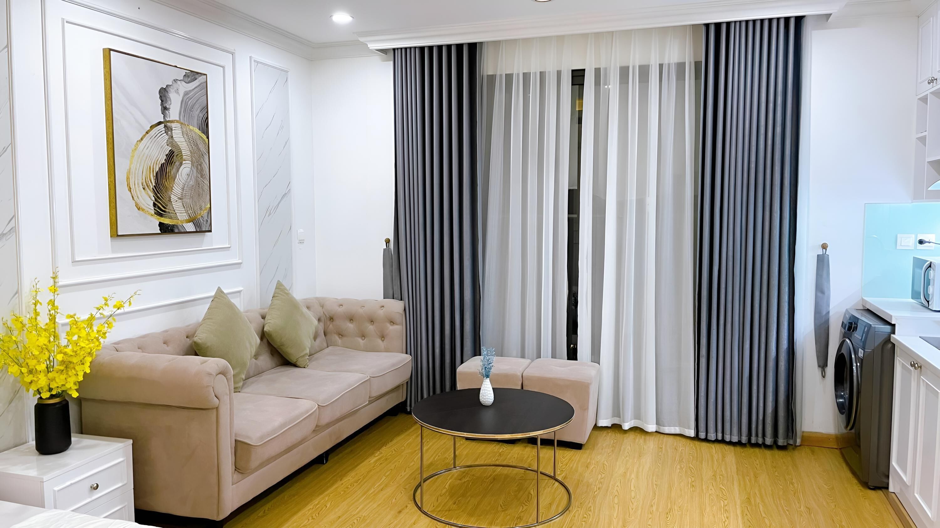 Een moderne woonkamer met een beige bank, een klein rond tafeltje en een groot raam met grijze gordijnen.