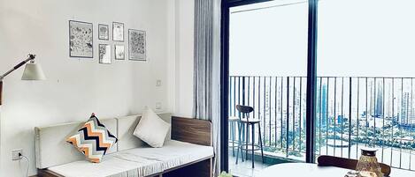 A modern living room with a sofa, a small table, and a balcony with a city view.