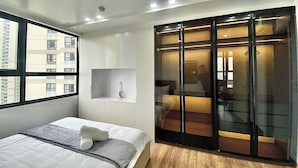 A modern bedroom with a bed, a built-in wardrobe, and a large window. - Vinhome D'capitale Service Apartment - Mikage Housing (Hanoi)
